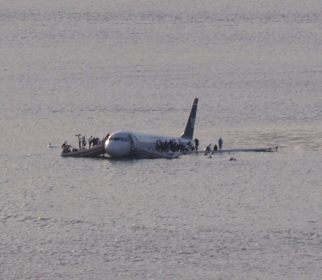 US Airways Flight 1549 floating in the Hudson River with passengers standing on the wings and in inflatable slide rafts, before rescue vessels arrived